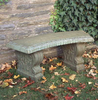 Curved green bench with decorative legs pictured against a stone wall covered with ivy