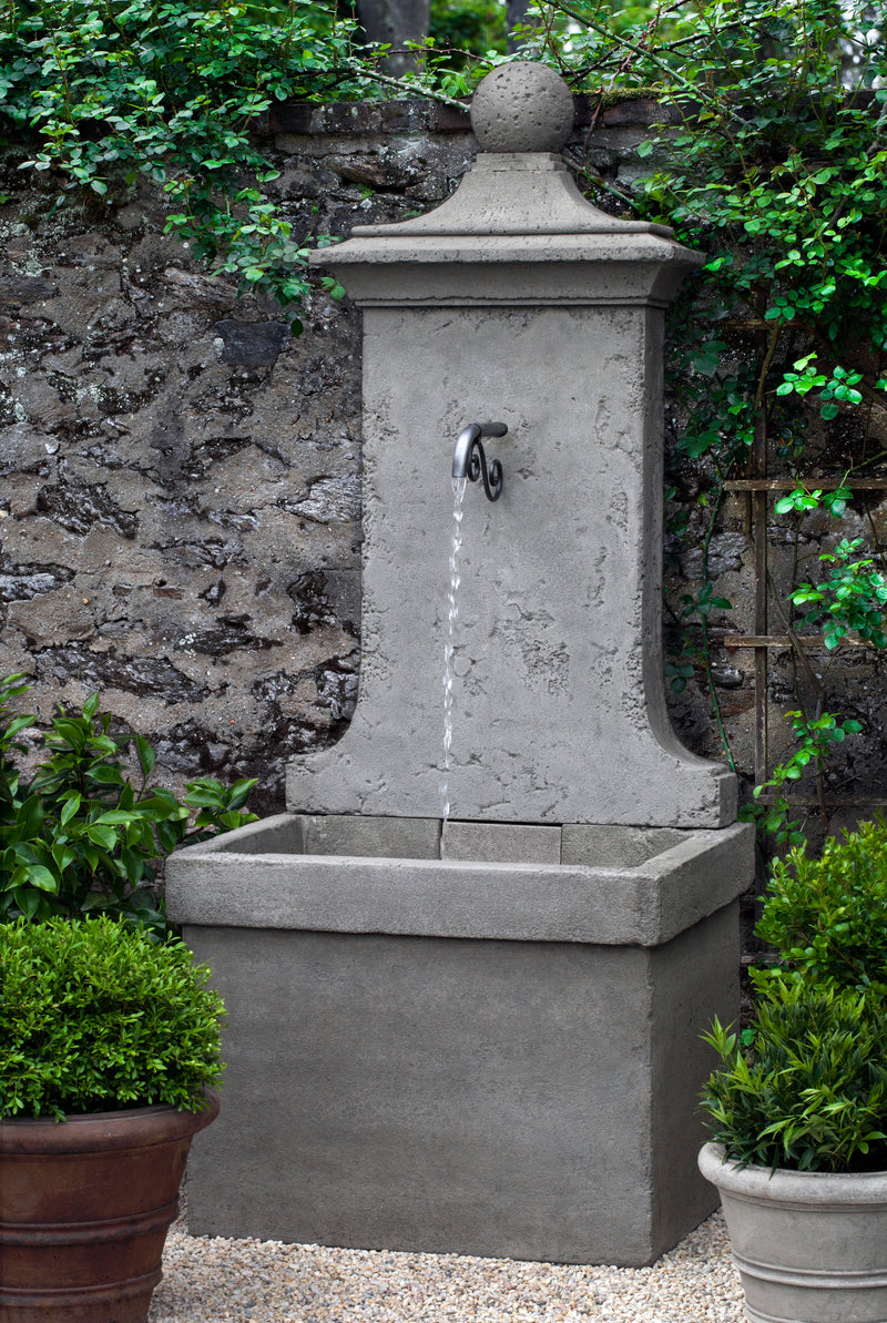 Traditional wall fountain with rectangular basin and one spout flowing into bottom basin pictured against ivy wall