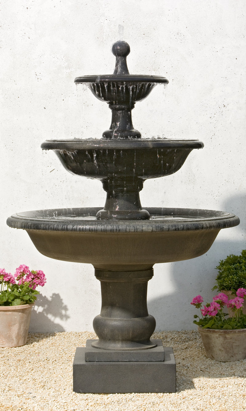 Black three tiered fountain with round finial pictured against white wall