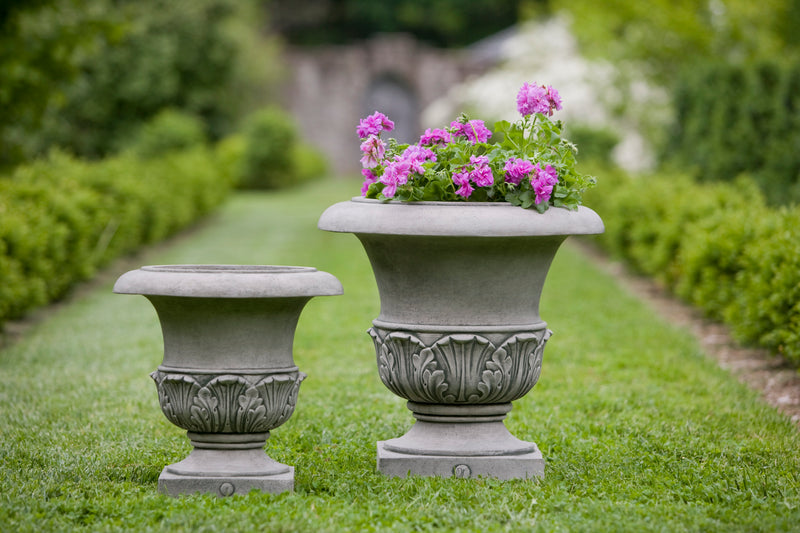 Two classic urns sitting on top of a lawn between a boxwood hedge