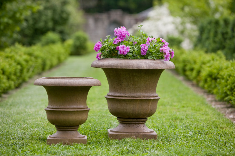 Two classic urns planted with purple geraniums and standing on a lawn