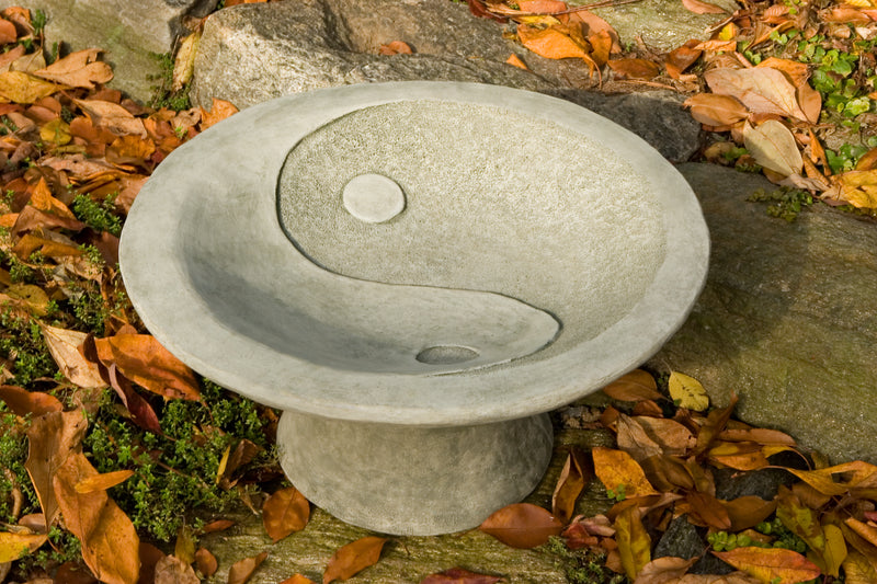 Small gray birdbath with yin yang design in bowl amongst autumn leaves