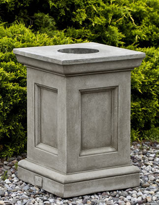 Square pedestal shown in front of evergreen shrub