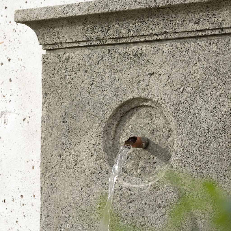 Detail of decorative fountain spout on grey fountain, placed against a white wall