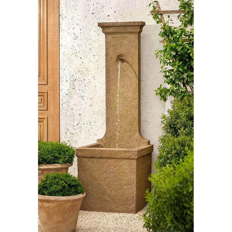 Brown wall fountain with one spout pictured with potted plants