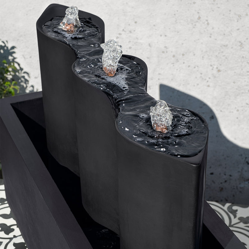 black fountain in rectangular basin with three oval columns and three copper spouts