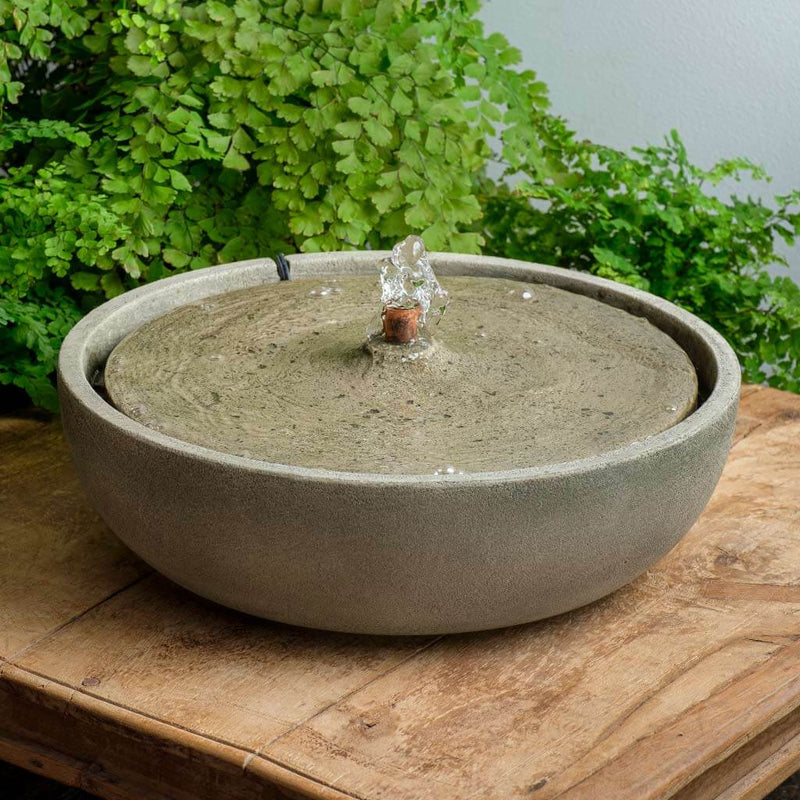 Tabletop fountain with circular top and copper spout in front of ferns