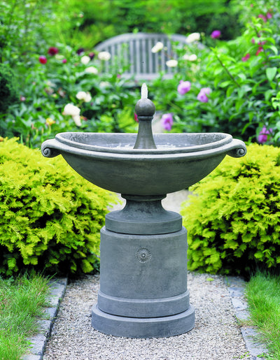 Free-standing fountain pictured running on gravel path with wooden bench in the background