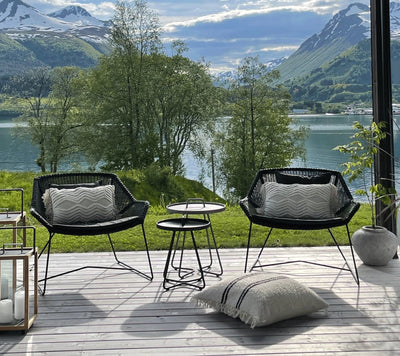 Set of two matching black woven outdoor armchairs with gray cushions in front of mountains and lake
