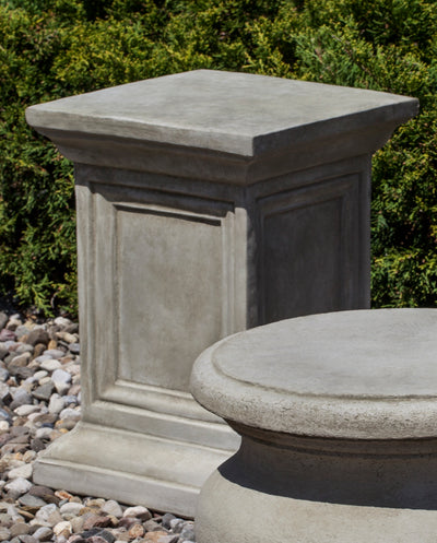 Square pedestal shown behind a round pedestal on gravel