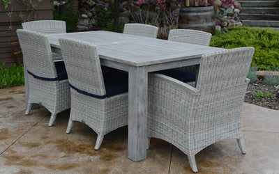 Rectangular gray teak table with six woven armchairs shown on light brown terrace