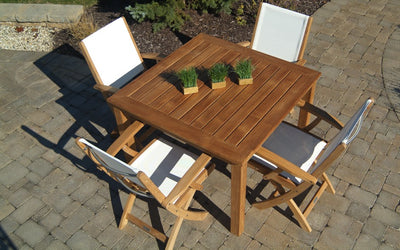 Teak table with four white chairs shown on paver patio