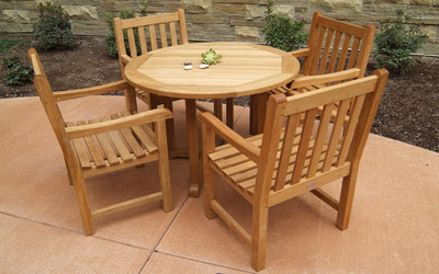 Round teak dining table with four armchairs shown in front of stone wall