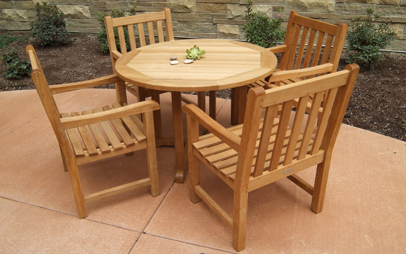 Round teak dining table with four armchairs shown in front of stone wall