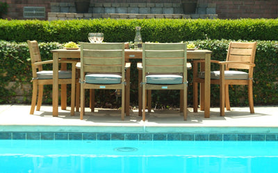 Rectangular teak table with six chairs shown behind a pool