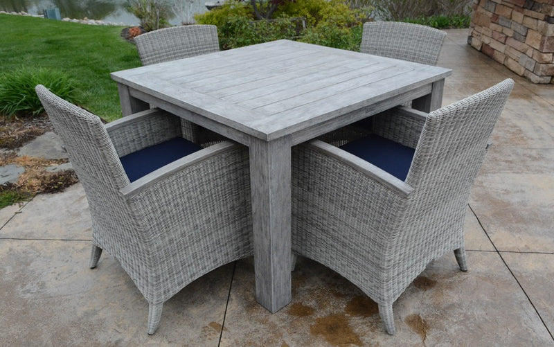 Square gray teak table with four woven armchairs shown on stone terrace