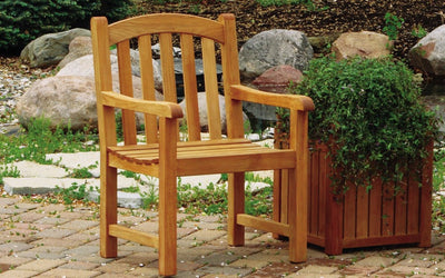 Teak armchair next to a planted wooden container on paver patio