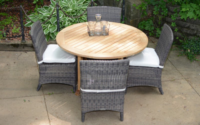 Round teak table with four woven chairs shown in front of hosta